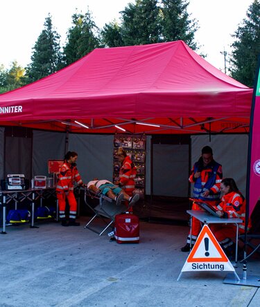Red 6x4 emergency tent with grey Rescue sidewalls and two custom teardrop flags with logo, used for an emergency simulation at a trade fair.
